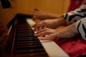 fechar-se fêmea pianista mãos criando a ritmo do melodia, tocante branco e Preto chaves do piano enquanto jogando piano com dela fofa filha, sentado perto em a borrado fundo foto