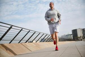 bonito desportista, Atlético homem corrida em a ponte em ensolarado dia, desfrutando dele manhã correr em a passeio foto