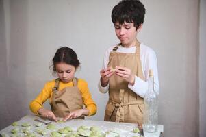 cozinhando classe para crianças. Garoto e menina preparando família jantar, em pé às enfarinhada cozinha mesa e modelagem dumplings ou ucraniano varennyky dentro a rural casa cozinha interior foto