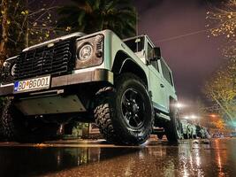 budva, Montenegro - 25 dezembro 2022. ampla branco suv carrinhos em a rua às noite dentro a iluminação do lanternas foto