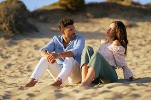 casal atraente sentado na areia da praia foto