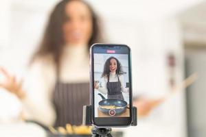 mulher latina gravando vídeo e cozinhando na cozinha foto