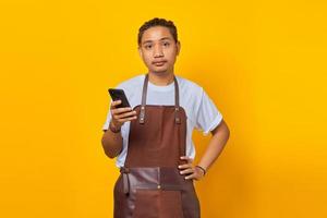 chocado bonito barista segurando um telefone celular e olhando para a frente em um fundo amarelo foto