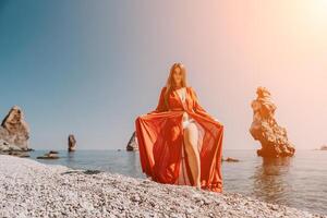 mulher viagem mar. feliz turista dentro vermelho vestir apreciar levando cenário ao ar livre para recordações. mulher viajante posando em a Rocha às mar baía cercado de vulcânico montanhas, partilha viagem aventura viagem foto