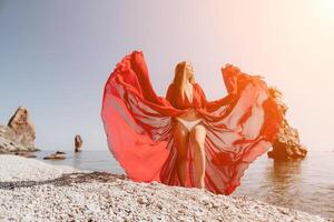 mulher viagem mar. feliz turista dentro vermelho vestir apreciar levando cenário ao ar livre para recordações. mulher viajante posando em a Rocha às mar baía cercado de vulcânico montanhas, partilha viagem aventura viagem foto