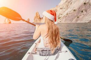 mulher dentro caiaque costas visualizar. feliz jovem mulher dentro santa chapéu flutuando dentro caiaque em calma mar. verão feriado período de férias e alegre fêmea pessoas relaxante tendo Diversão em a barco. foto