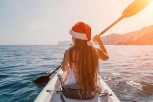 mulher dentro caiaque costas visualizar. feliz jovem mulher dentro santa chapéu flutuando dentro caiaque em calma mar. verão feriado período de férias e alegre fêmea pessoas relaxante tendo Diversão em a barco. foto