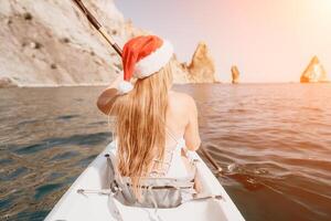 mulher dentro caiaque costas visualizar. feliz jovem mulher dentro santa chapéu flutuando dentro caiaque em calma mar. verão feriado período de férias e alegre fêmea pessoas relaxante tendo Diversão em a barco. foto