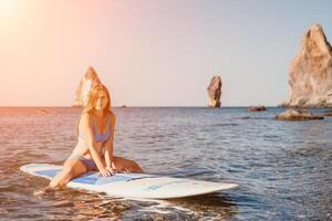 mulher mar e aí. fechar acima retrato do feliz jovem caucasiano mulher com grandes cabelo olhando às Câmera e sorridente. fofa mulher retrato dentro uma azul bikini posando em sup borda dentro a mar foto