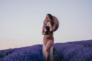 mulher lavanda campo. feliz despreocupado mulher dentro bege vestir e chapéu com ampla borda cheirando uma florescendo lavanda em pôr do sol. perfeito para inspirado e caloroso conceitos dentro viagem e desejo de viajar. fechar acima foto