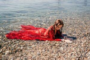 mulher viagem mar. feliz turista dentro vermelho vestir apreciar levando cenário ao ar livre para recordações. mulher viajante posando dentro mar praia, cercado de vulcânico montanhas, partilha viagem aventura viagem foto