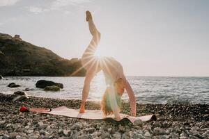 mulher mar ioga. feliz mulher dentro branco roupa de banho e boho estilo braquetes praticando ao ar livre em ioga esteira de mar em pôr do sol. mulheres ioga ginástica rotina. saudável estilo de vida, harmonia e meditação foto