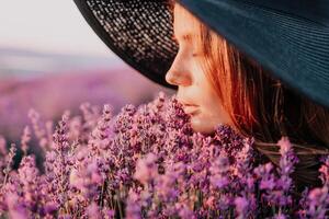 mulher lavanda campo. feliz despreocupado mulher dentro Preto vestir e chapéu com ampla borda cheirando uma florescendo lavanda em pôr do sol. perfeito para inspirado e caloroso conceitos dentro viagem e desejo de viajar. fechar acima foto