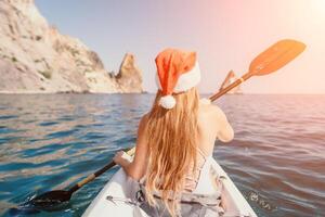 mulher dentro caiaque costas visualizar. feliz jovem mulher dentro santa chapéu flutuando dentro caiaque em calma mar. verão feriado período de férias e alegre fêmea pessoas relaxante tendo Diversão em a barco. foto