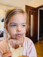 pequeno menina com uma sujo face senta com chocolate gelo creme dentro uma waffle copo foto