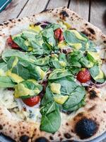 pizza com espinafre, queijo e tomates carrinhos em a mesa foto