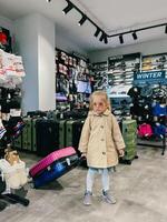 budva, Montenegro - 18 dezembro 2023. pequeno menina dentro oculos de sol carrinhos dentro uma loja segurando uma viagem mala de viagem de a lidar com foto