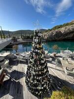lustica, Montenegro - 25 dezembro 2022. Natal árvore fez do vinho garrafas carrinhos perto mesas com cadeiras em a Beira Mar foto