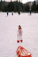 pequeno menina carrinhos em a neve segurando uma corda dentro dela mão foto