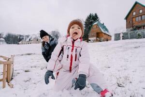 sorridente mãe olhando às pequeno menina ajoelhado em Nevado Colina e degustação neve foto