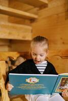 pequeno menina lendo uma livro com dela boca aberto enquanto sentado em uma de madeira cadeira foto