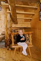 pequeno menina abraços uma suave brinquedo enquanto sentado em uma de madeira cadeira perto a escadas dentro uma chalé foto
