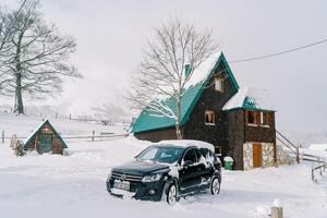 coberto de neve Preto suv carrinhos perto uma de madeira duas histórias chalé dentro a Vila foto