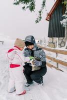 pequeno menina golpes uma malhado gato dentro dela mãe agachado braços em uma Nevado Vila estrada foto