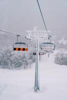 quatro pessoas teleférico assentos mover ao longo uma cabo acima uma coberto de neve lado da montanha foto