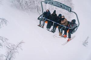 esquiadores dentro esqui equipamento ir morro acima em uma teleférico acima coberto de neve árvores foto