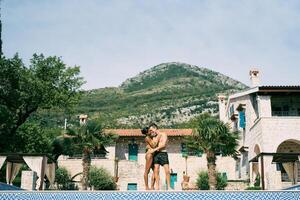 homem e mulher abraço enquanto em pé de a piscina dentro frente do a antigo villa foto