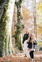 mãe segue uma pequeno menina roendo a maçã dentro a outono floresta foto