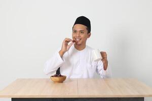 retrato do animado ásia muçulmano homem comendo kurma ou encontro fruta durante sahur e quebra rápido. cultura e tradição em Ramadã mês. isolado imagem em branco fundo foto