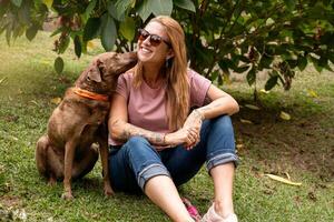 uma sorridente mulher e dela adorável cachorro em a verde Relva dentro a parque. foto