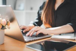 fechar-se do uma mulher mãos digitando em uma computador portátil teclado, com bloco de anotações e caneta em a mesa, destacando produtividade e organização. foto