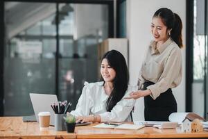 uma sentado mulher trabalho atentamente às dela computador portátil enquanto dela colega carrinhos ao lado dela, gesticulando de forma solidária, representando uma momento do trabalho em equipe dentro uma moderno escritório contexto. foto