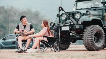 casal é profundo dentro conversação, desfrutando uma caloroso beber enquanto sentado ao lado uma áspero fora da estrada carro às seus cênico acampamento. foto