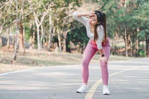 jovem mulher dentro roupa de esporte pausas para uma descansar durante uma corre dentro uma parque, limpando suor a partir de dela testa. foto