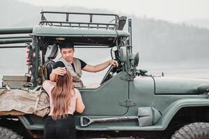 carinhoso homem assistências uma mulher Como ela sobe para dentro uma robusto fora da estrada carro para a aventura de uma enevoado lago às alvorecer. foto