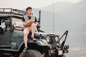 pensativo jovem homem detém uma caderno enquanto sentado em uma áspero carro, contemplando dele Próximo aventura dentro a região selvagem. foto