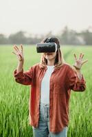 dentro uma verdejante arroz campo às crepúsculo, uma mulher com uma vr fone de ouvido alcança fora, explorando uma digital mundo além a natural panorama. foto