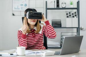 mulher dentro uma listrado vermelho e branco camisa é sentado às dela mesa, interagindo com uma virtual realidade fone de ouvido, dela esquerda índice dedo aguçado para cima. foto