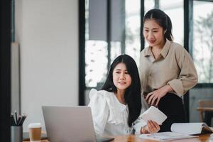 o negócio equipe analytics conceito, alegre ásia mulheres de negócios partilha documentos e Ideias às uma colaborativo escritório área de trabalho com uma computador portátil. foto