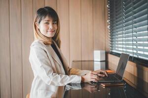 uma confiante jovem profissional trabalho em dela computador portátil de uma janela com persianas, dela preparado comportamento refletindo eficiência e ambição dentro uma corporativo contexto. foto