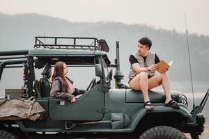uma jovem homem e mulher noivando dentro conversação enquanto planejamento seus jornada, sentado em uma áspero, equipado jipe ao ar livre. foto