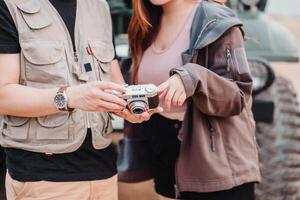 jovem casal carrinhos juntos ao ar livre, partilha uma momento sobre uma vintage Câmera com uma carro dentro a fundo. foto