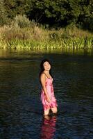 jovem japonês mulher em pé dentro rio sorridente molhado vestir foto