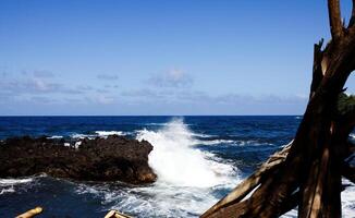 azul oceano e céu com ondas falhando em Preto lava Rocha foto