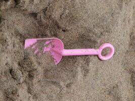 pequeno plástico Rosa pá deitado dentro areia foto