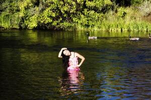 sorridente japonês americano mulher em pé dentro rio com gansos foto